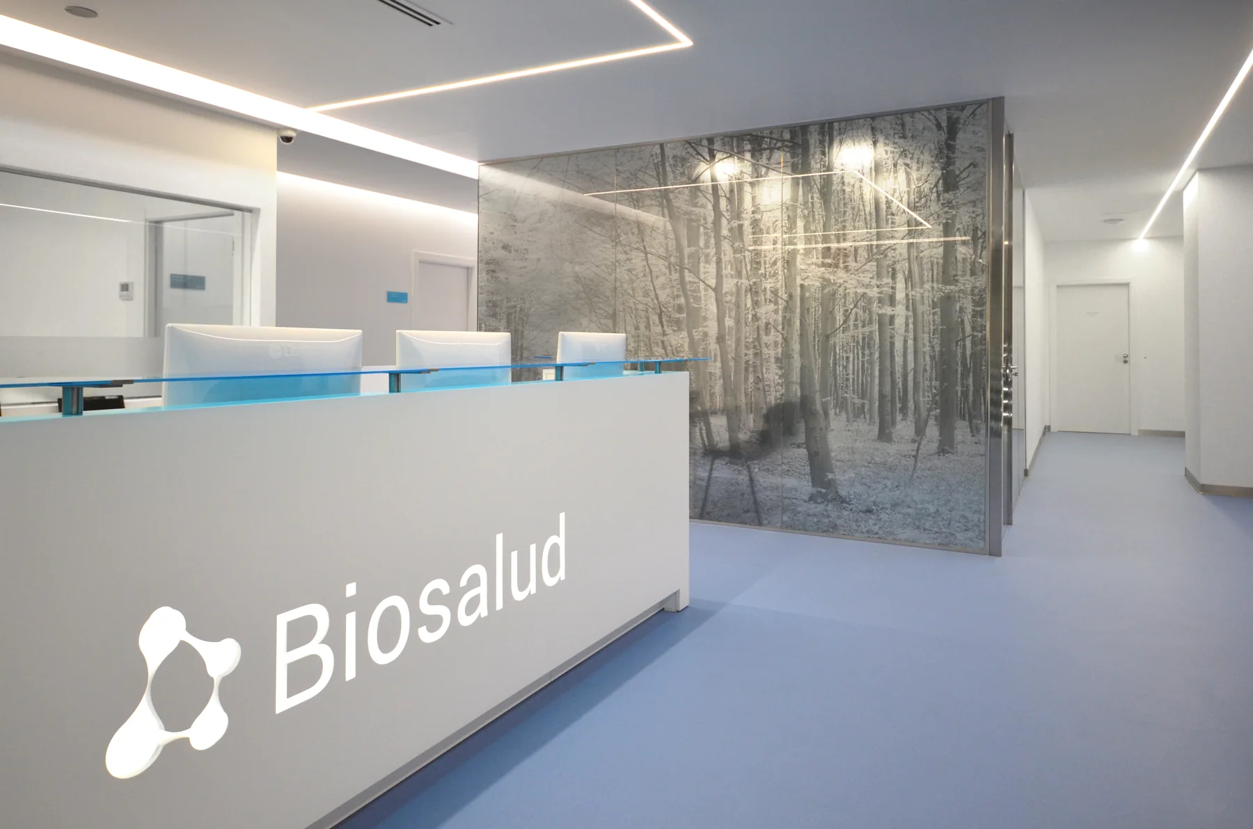 Recepción de Biosalud con mostrador blanco y paneles con imagen de bosque.