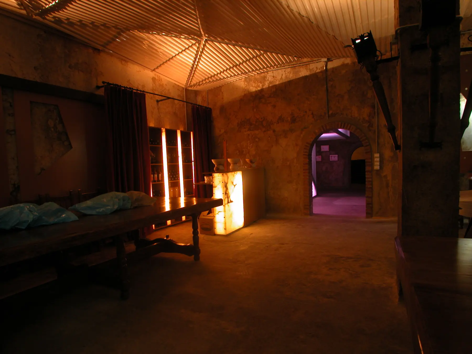 Interior de la bodega con muros de textura irregular, techo de lamas e iluminación cálida.