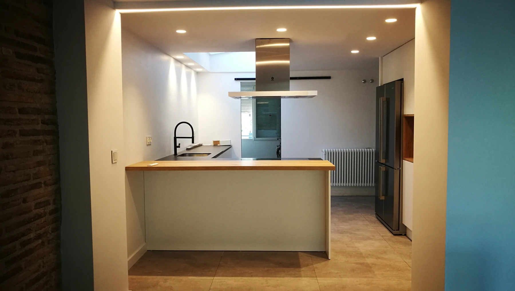 Cocina con península, campana central e iluminación integrada en el techo.