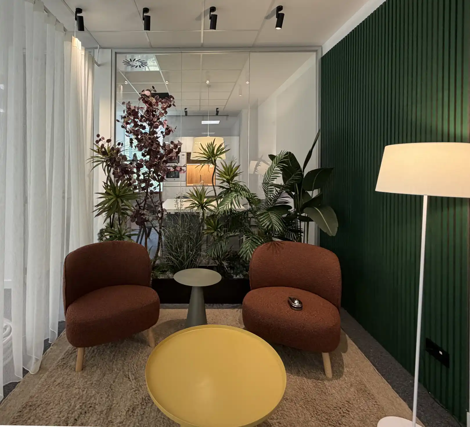 Rincón de descanso con butacas marrones, mesa amarilla y pared verde en Oficinas Madrid.