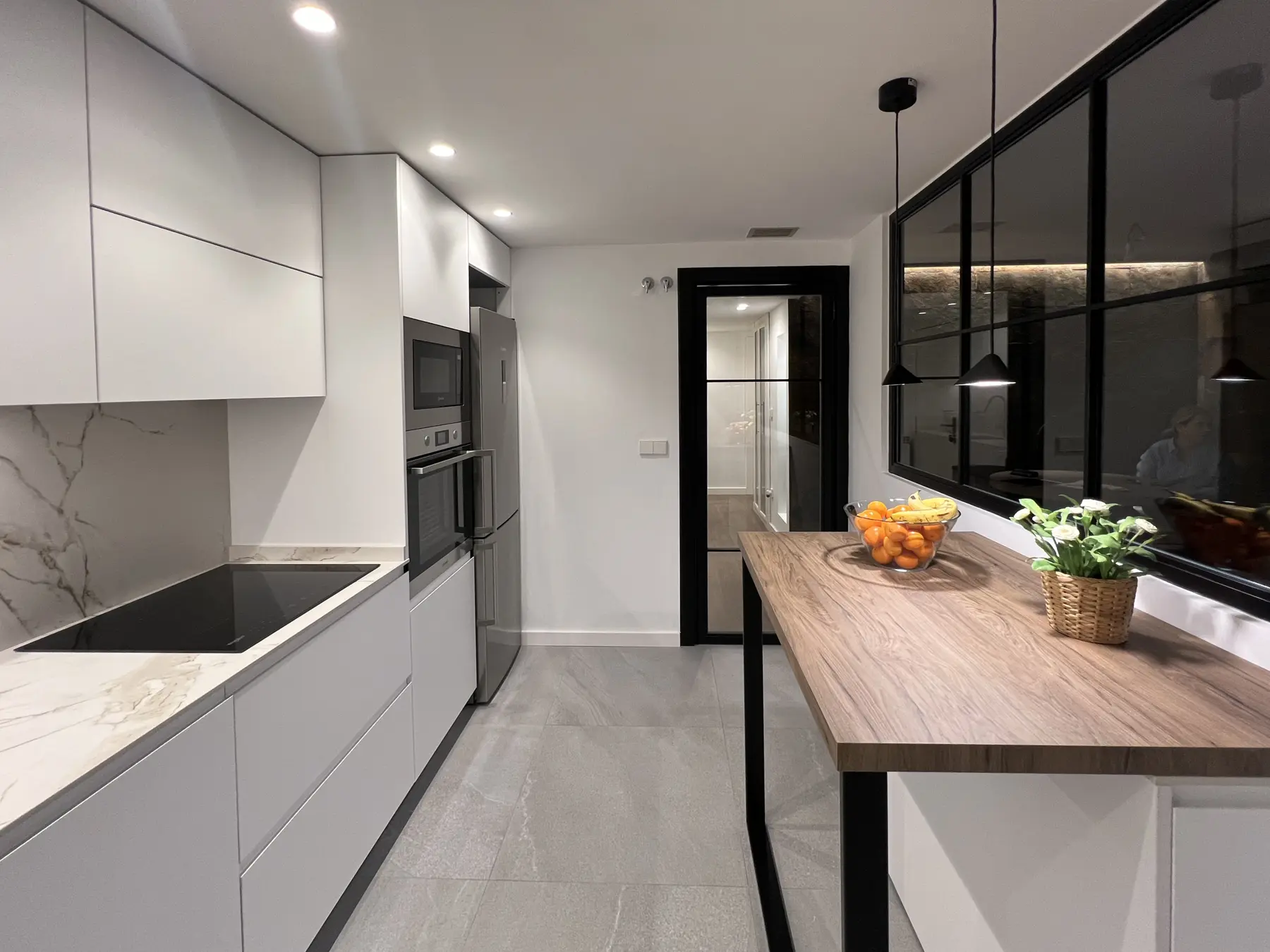 Cocina blanca con barra de madera junto al cerramiento acristalado.