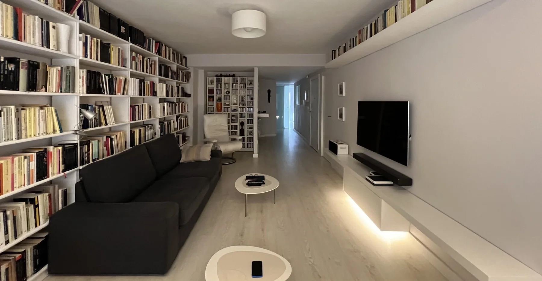 Salón con sofá negro, gran librería y mueble de televisión con iluminación inferior.