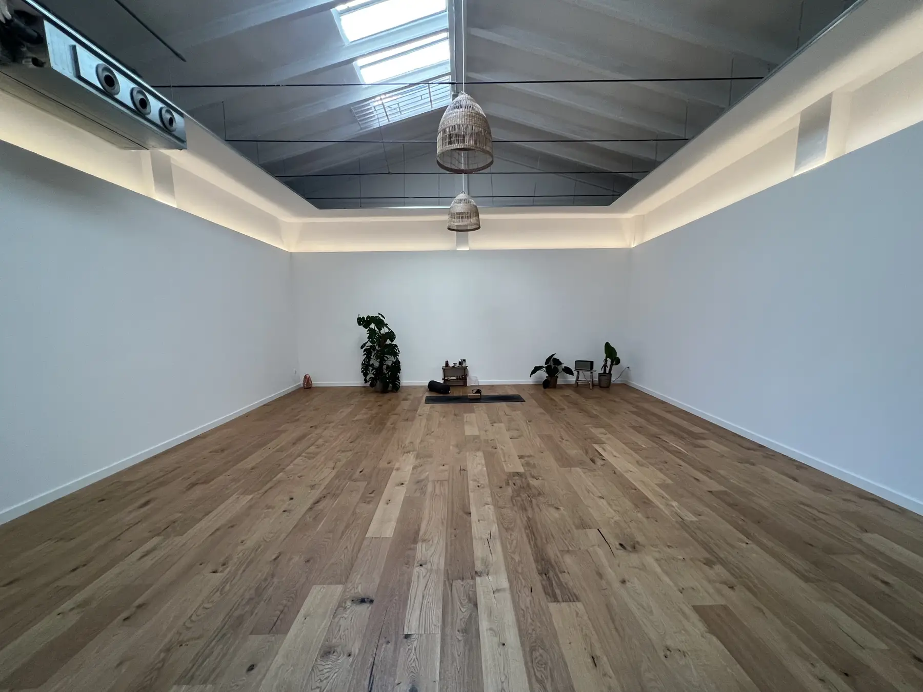 Sala de yoga con suelo de madera, paredes blancas y luz cenital.