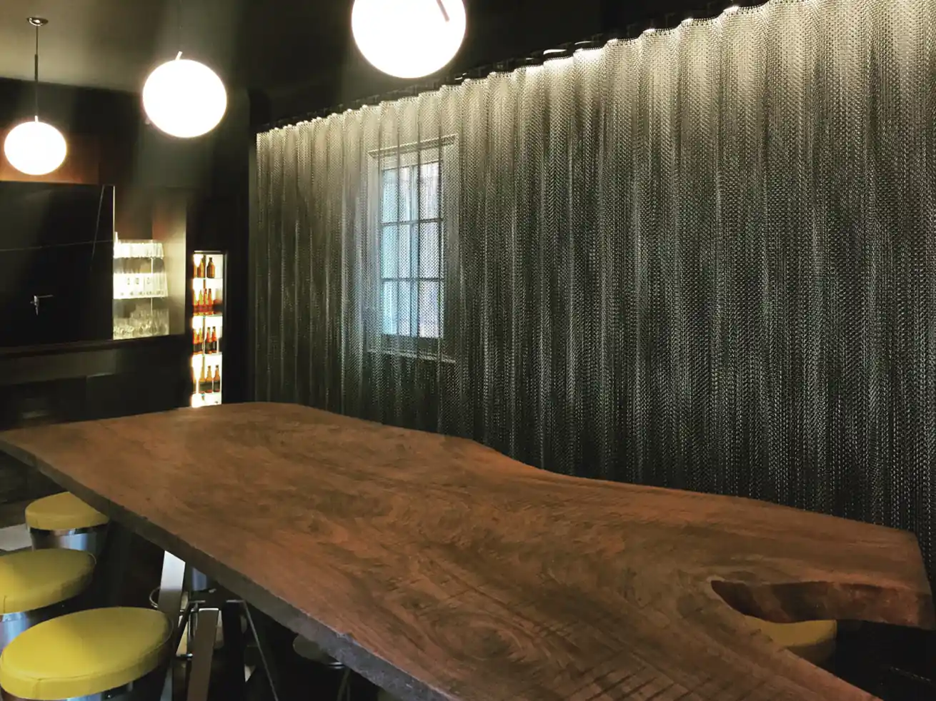 Gran mesa de madera bajo lámparas esféricas y junto a cortinas de cadenas.